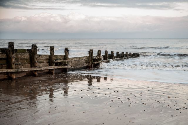 Peaceful image of weathered wooden groynes stretching into the calm sea with gentle waves hitting the shore. Suitable for promoting coastal tourism, relaxation themes, or erosion study materials. Ideal for background images or blog headers addressing travel, nature, and scenic views.