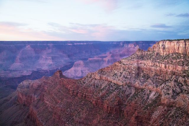 Depicts Grand Canyon at sunset surrounded by majestic red rock formations. Ideal for travel brochures, nature photography websites, educational materials on geological formations, and marketing materials for tourism in the American Southwest.