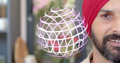 Smiling man wearing red turban interacting with holographic orb in modern office