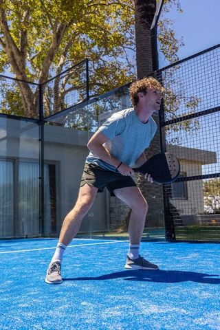 Male padel player holding racket preparing to return on bright blue outdoor court