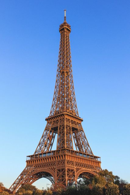 Eiffel Tower rising against a clear blue sky during sunset, highlighting its intricate ironwork. Ideal for promoting travel to Paris, illustrating iconic landmarks, and depicting architectural marvels.