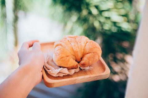 Hand holding croissant on wooden plate with outdoor background
