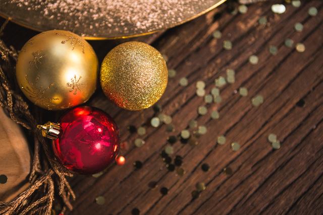 Christmas baubles in gold and red colors placed on a wooden plank with glitter scattered around. Ideal for holiday greeting cards, festive invitations, seasonal promotions, and Christmas-themed blog posts.