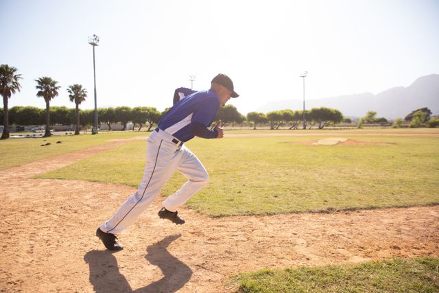 Male baseball player running on a baseball field during a game on a sunny day. Ideal for use in sports-related content, athletic training materials, fitness promotions, and outdoor activity advertisements. Perfect for illustrating teamwork, competition, and athleticism.