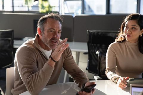 Manager discussing project while holding phone and colleague using tablet in modern office