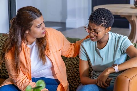 Friend comforting upset african american woman on sofa showing empathy and support