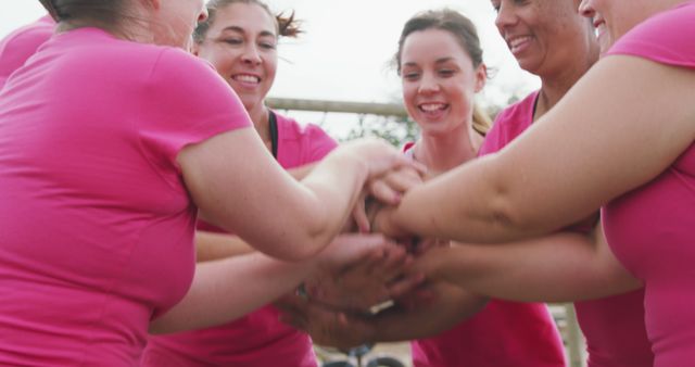 Happy caucasian female friends in pink t shirts stacking hands after cross training at bootcamp. Female fitness, challenge, friendship and healthy lifestyle.