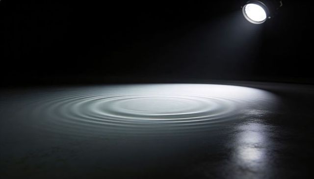 Spotlight highlighting concentric water ripples on glossy surface minimal monochrome concept