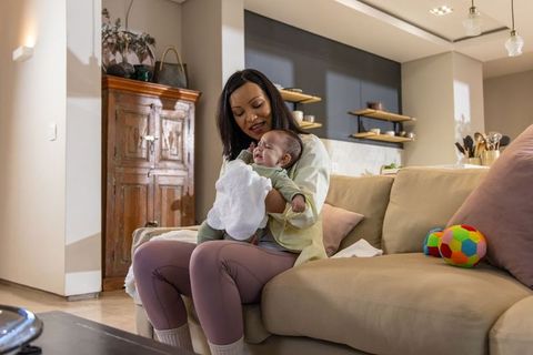 Mother soothing crying infant on sofa with burp cloth in cozy modern living room