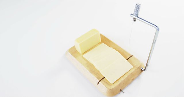 A block of butter is being sliced with a metal wire cutter on a wooden board, with copy space. This kitchen tool provides a clean and efficient way to cut even slices for cooking or serving.