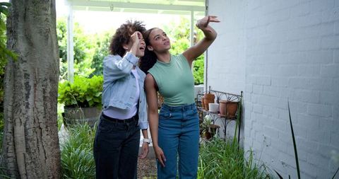 African american women pointing upward on garden path beside white brick wall in denim