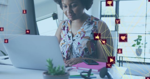 African American woman working on a laptop in a modern office setting with social media icons overlayed. Ideal visual for concepts related to multitasking, social media marketing, remote work, and technology usage.