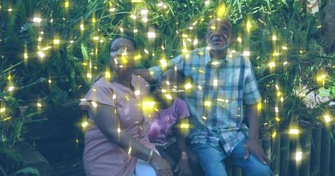 Grandparents and granddaughter sitting on bench with golden light overlay in lush garden