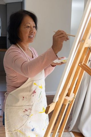 Senior Asian Woman Painting at Home on Wooden Easel