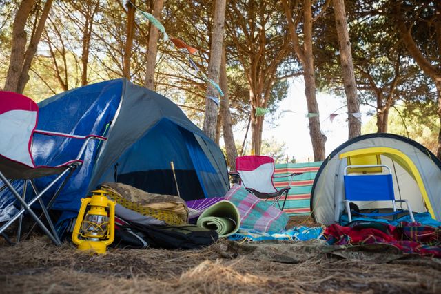 Camping gear including tents, chairs, and lantern set up in a forest on a sunny day. Ideal for use in content related to outdoor activities, adventure travel, camping tips, nature exploration, and family vacations.