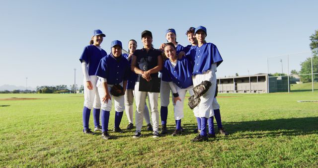 Group portrait of diverse team of female baseball players and coach standing on sunny pitch smiling. female baseball team, sports training and game tactics.