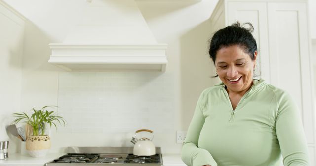 Elderly woman standing in bright kitchen, showing joy while cooking. Captures essence of relaxed domestic life. Useful for illustrating senior balanced lifestyle, retirement activities, contentment, and promoting healthy home cooking habits.