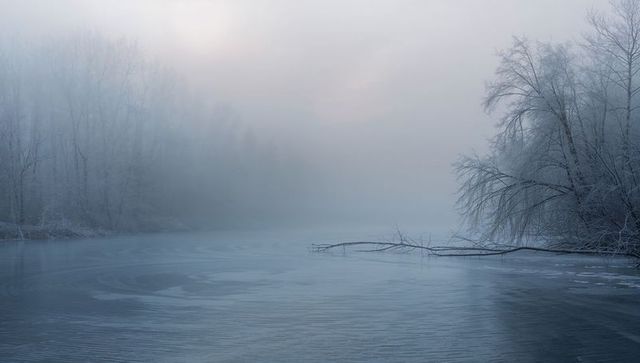 Misty frozen river at dawn with frosted trees, fallen branch and rippling thin ice