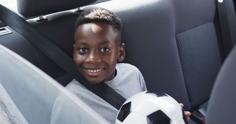 Excited Boy Holding Soccer Ball in Backseat