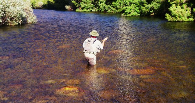 Man stands in river fly-fishing, surrounded by greenery. Perfect for themes of outdoor recreation, fishing, nature adventures, summertime activities, and tranquil landscapes. Use for travel blogs, fishing gear advertisements, or conservation campaigns.