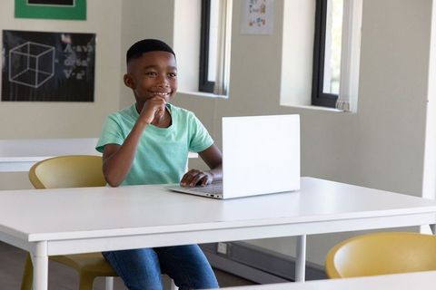African american boy smiling using laptop in modern classroom studying geometry and coding
