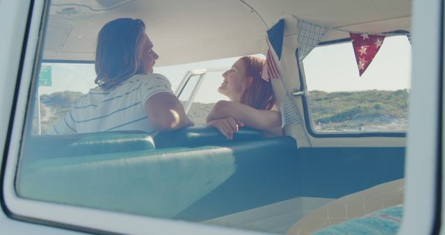 Couple seated inside a retro camper van during a road trip. They appear happy, engaged in conversation, and enjoying each other's company. Scenery through window hints at a beachside or nature setting. Perfect for campaigns about travel, vacations, freedom, lifestyle, and bonding experiences.