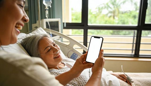 Senior asian woman recovering in hospital bed smiling while family shares smartphone