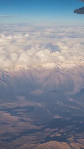 Vertical video cruising over snow-capped peaks through low cloud band from aircraft window