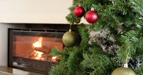 Christmas tree with baubles by cozy fireplace