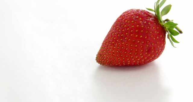 Single ripe strawberry on a white background highlighting its fresh, organic goodness. Ideal for promoting healthy eating, fruit-based products, organic farming, vegetarian diet, and dessert recipes.