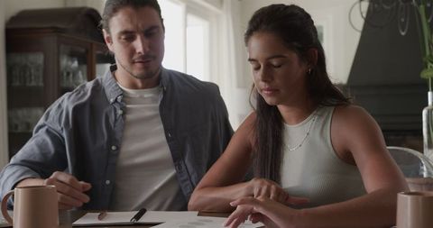 Couple planning wedding, discussing documents at home for celebration
