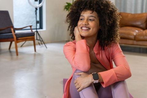 African american woman sitting and smiling on purple yoga mat in modern home studio