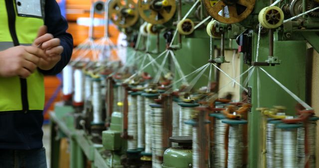 Worker operates textile spinning machine in modern factory. Image ideal for articles or content focused on the industrial manufacturing process, textile production, or advancements in factory technology.