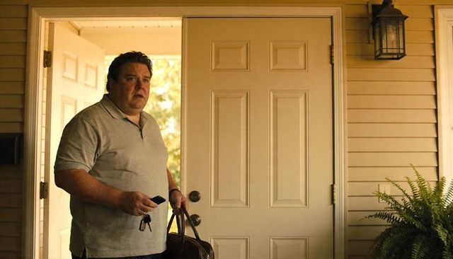 Standing man holding keys and leather duffel at suburban front door