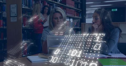 Female students collaborating on laptop with binary code overlay in library