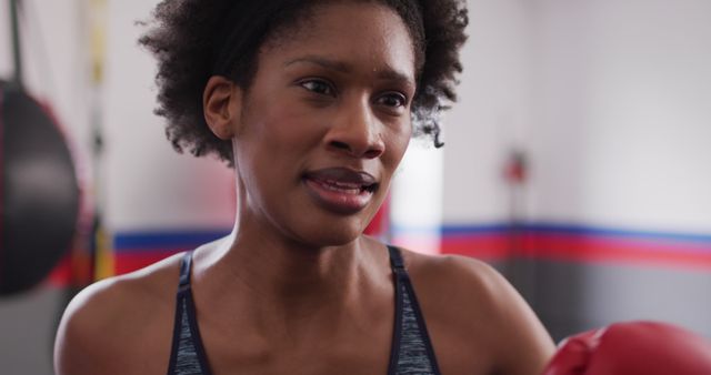 Image of confident, determined african american woman in boxing gloves training with punchbag at gym. Exercise, fitness and healthy lifestyle.