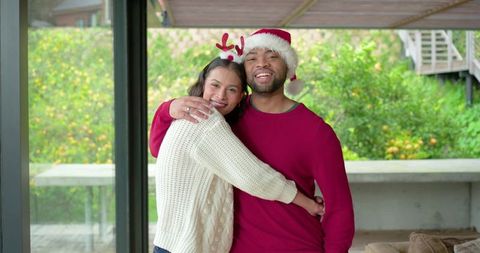 African american couple hugging on patio wearing santa hat and reindeer headband