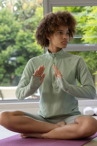 Young woman practicing seated mindfulness breathing on mat by window in serene home yoga