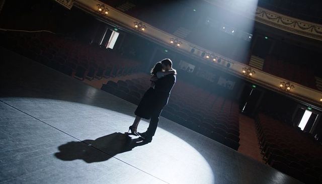 Romantic couple embracing on empty theater stage under dramatic circular spotlight