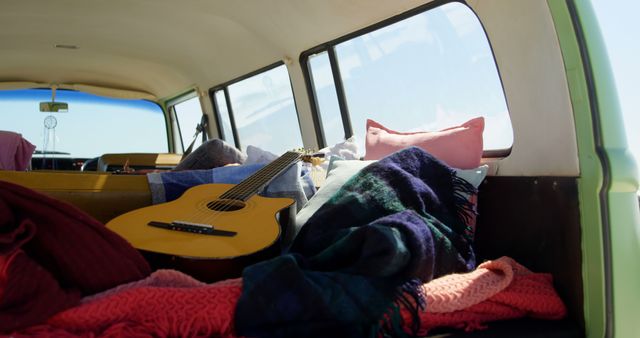 Interior of a cozy camper van adorned with a guitar and colorful blankets, creating a comfortable and relaxed atmosphere. Ideal for promoting road trips, travel adventures, camping experiences, or bohemian and retro lifestyles.