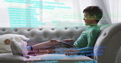Young boy reclining on sofa using tablet with code overlay learning to code at home
