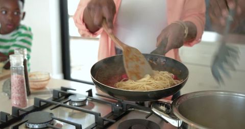 African american mother stirring pasta in bright modern kitchen while child watches