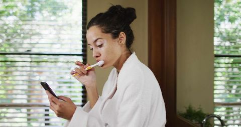 Woman Brushing Teeth While Checking Smartphone in Bathroom