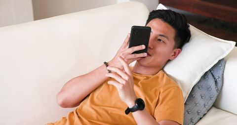 Young asian man relaxing on sofa using smartphone at home