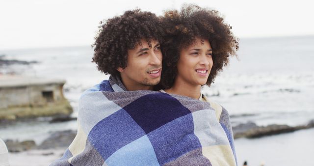 African american couple wrapped in blanket on the promenade near the beach. love and relationship concept