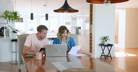 Joyful Couple Celebrating Paperwork Success in Home Dining Area