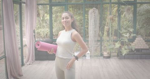 Holding Pink Yoga Mat in Sunroom Surrounded by Lush Plants Wearing Neutral Activewear and Smartwatch