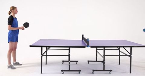 Female table tennis player ready to compete on purple table in studio