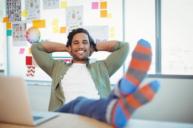 Male graphic designer relaxing with feet up at desk in office