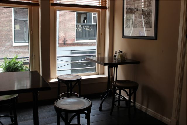 Showcasing the comfortable atmosphere of a cafe with minimalist wooden furniture and large windows offering a view of the streets. Ideal for use in marketing materials for cafes, urban lifestyle blogs, hospitality designs, or ambience presentations.